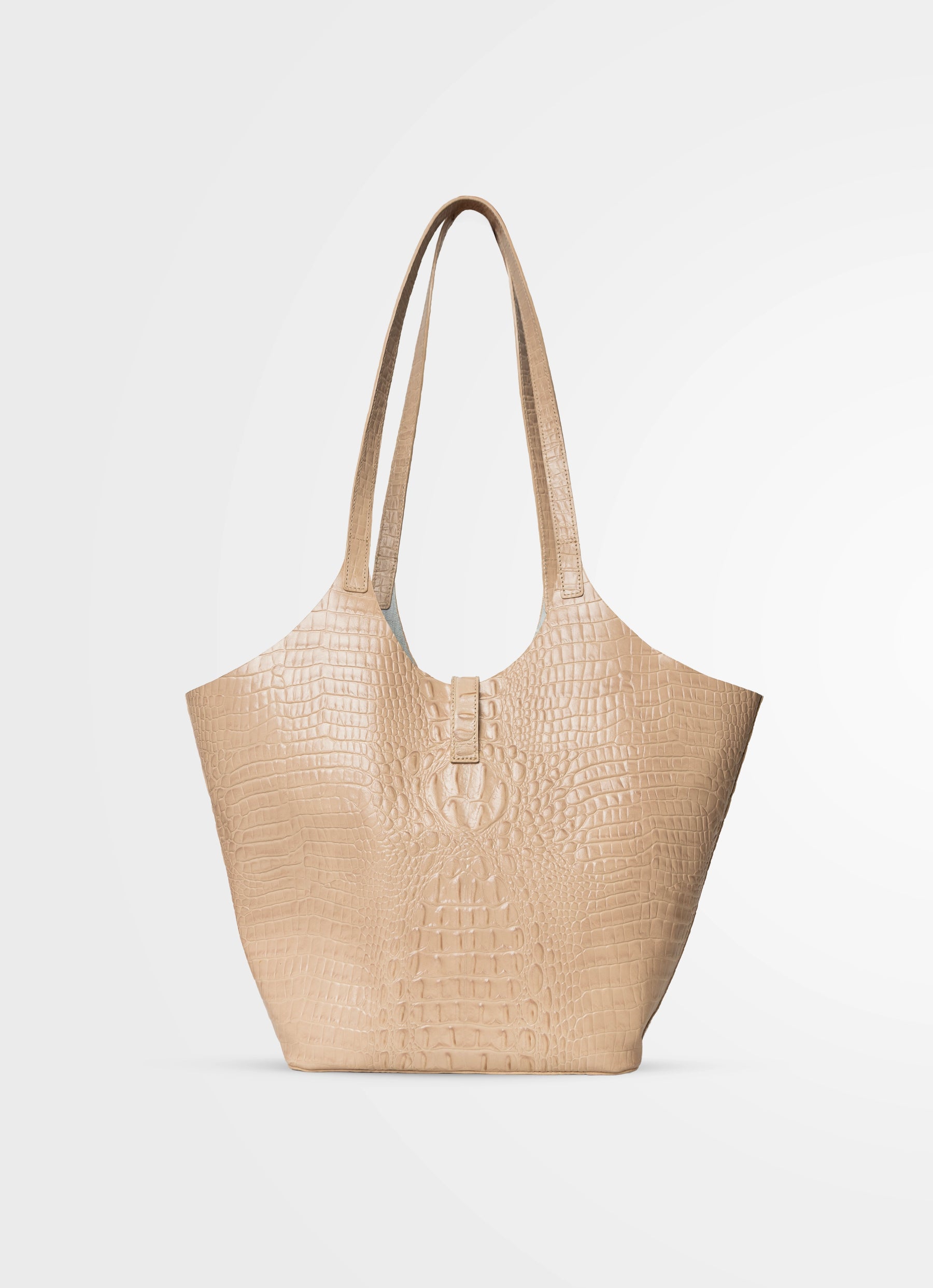 A light beige tote bag with a crocodile-embossed texture, featuring two shoulder straps and a small front buckle detail, set against a plain light gray background.