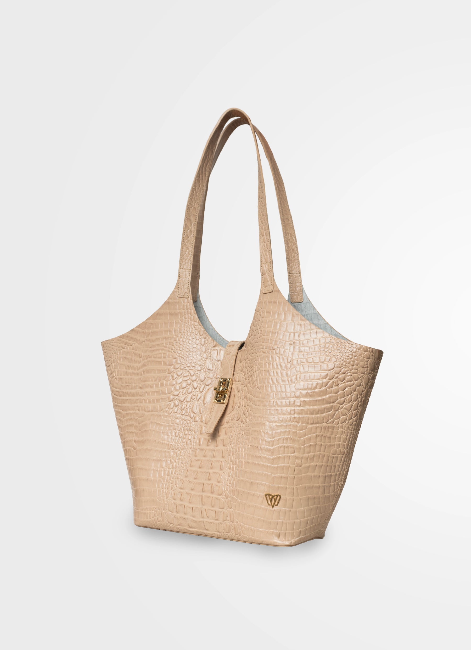 A structured beige tote bag with an embossed crocodile pattern, dual shoulder straps, a small gold clasp, and a gold logo emblem near the bottom right, shown on a light gray background.